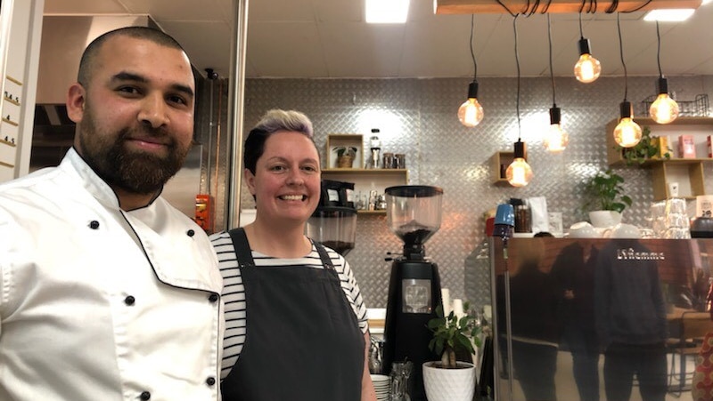 Christine Medson and Milan Gnawali stand in their cafe in front of coffee machine