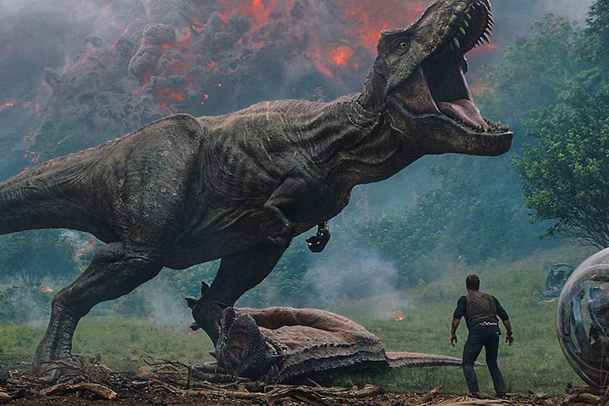 Chris Pratt's character is diminished by an enormous t-rex standing in front of an erupting volcano.