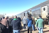 Auctioneers stand in front of a train at Canberra railway auction.