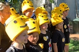 A group of school children with foam Lego man hats smiles while posing for a photo outside.