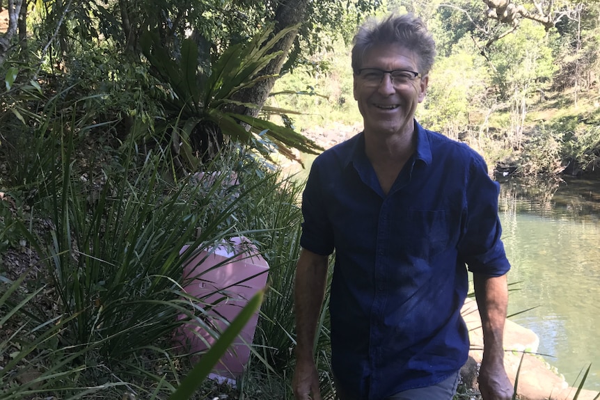 Steven Lang smiling at the camera in front of a beautiful creek and new screens around plantings.