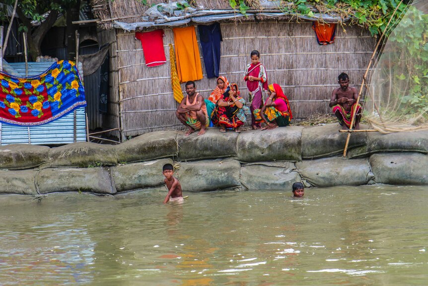 Kids play in floodwaters as adults watch on.