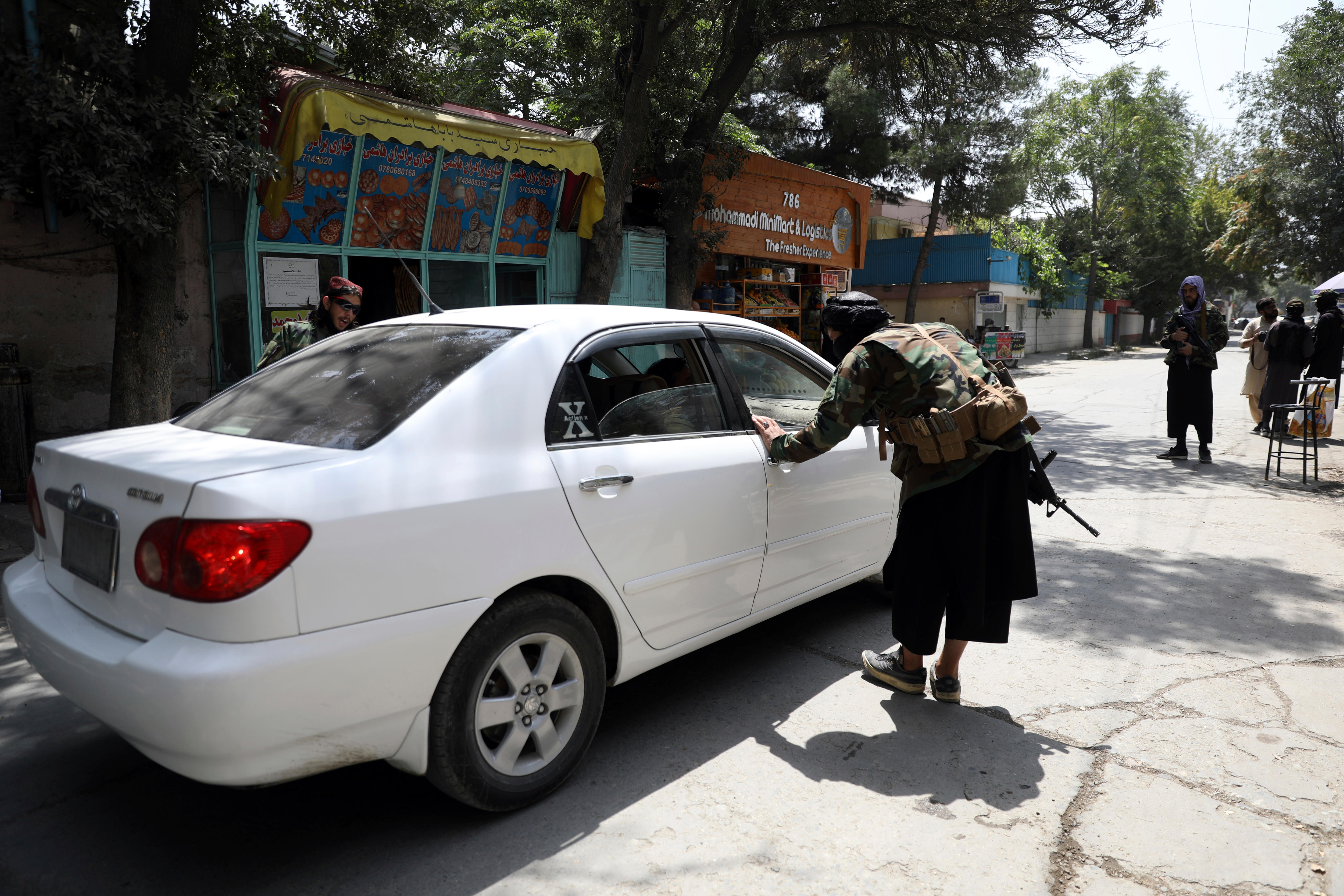 Taliban fighters search a vehicle at a checkpoint in Kabul