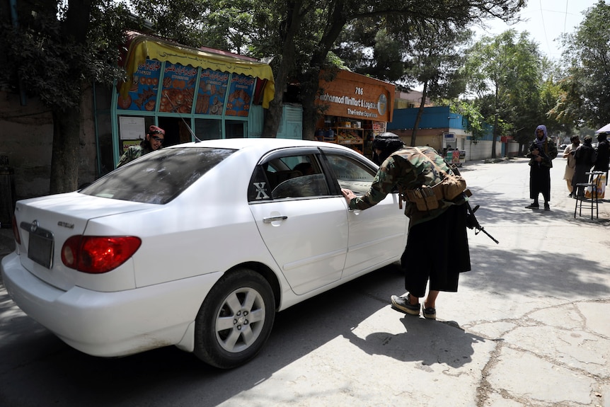 Taliban fighters search a vehicle at a checkpoint in Kabul