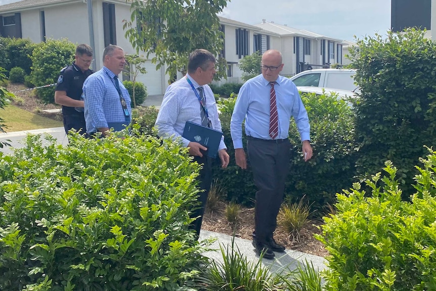 Three police detectives walk through hedges.