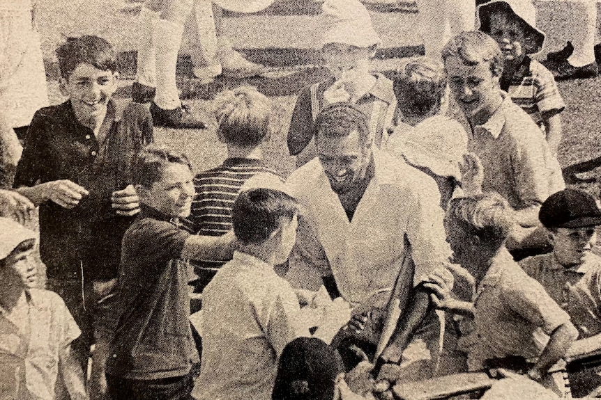 A cricketer being swamped by young fans.