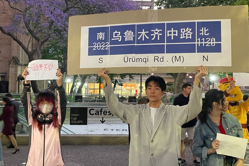 A young Chinese male holds a protest sign saying Urumqui Road.  