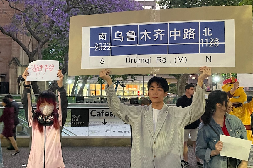 A young Chinese male holds a protest sign saying Urumqui Road.  