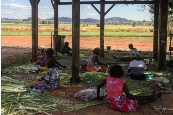 Ladies sit down stripping pandanus, before it will be dyed and woven into baskets.