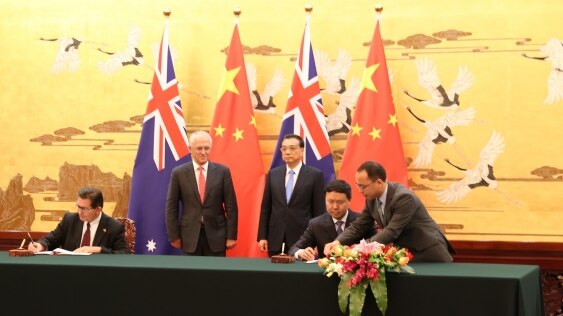 Ian Jacobs and a Chinese colleague sign documents in front of Malcolm Turnbull and Li Keqiang.
