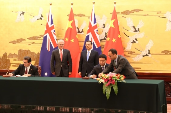 Ian Jacobs and a Chinese colleague sign documents in front of Malcolm Turnbull and Li Keqiang.