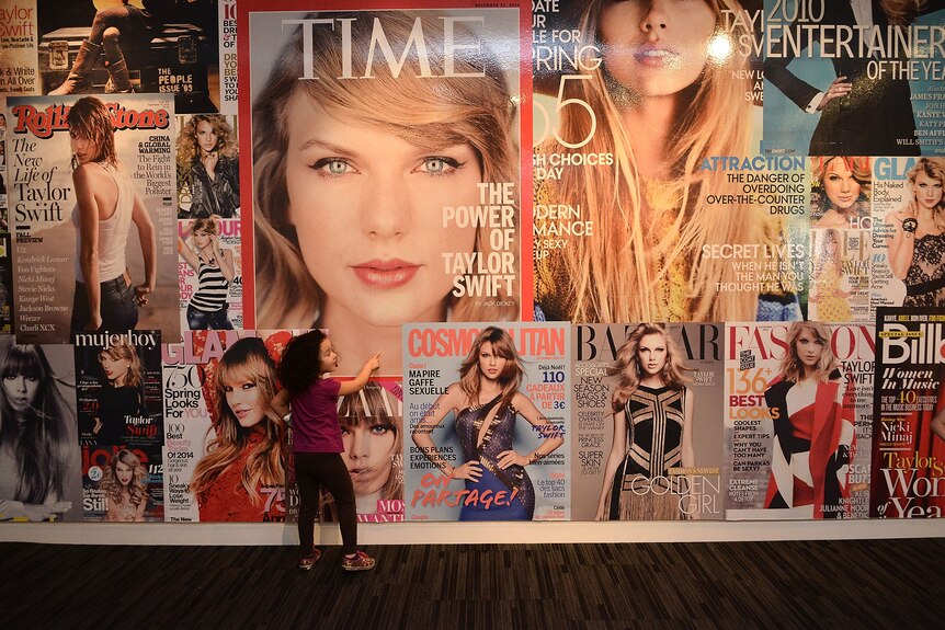 A wall of magazine covers of Taylor Swift, including a large image of her Time magazine cover.