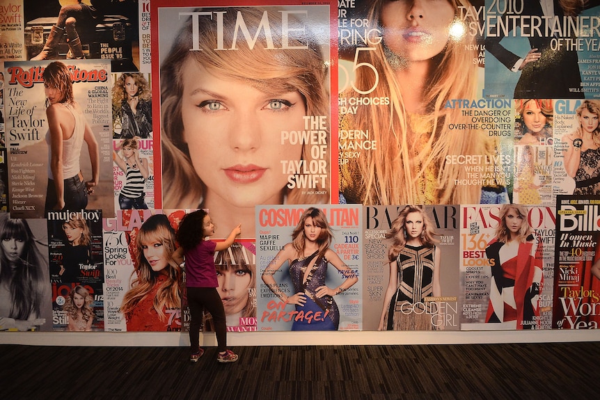 A wall of magazine covers of Taylor Swift, including a large image of her Time magazine cover.