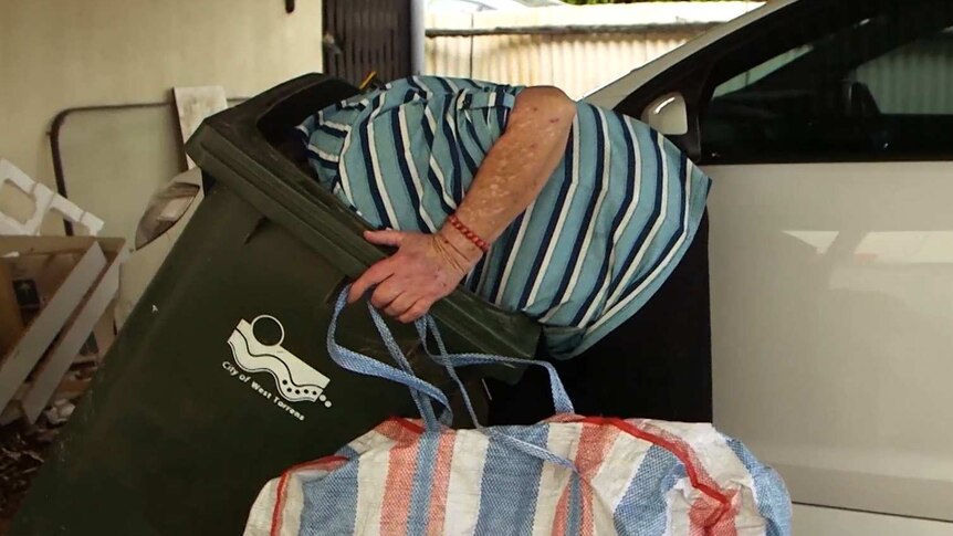Joan goes through a recycling bin to find cans and bottles.