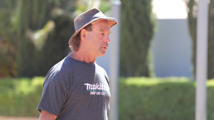 A man in wide-brim hat walking into a police station to report for bail for trial.  