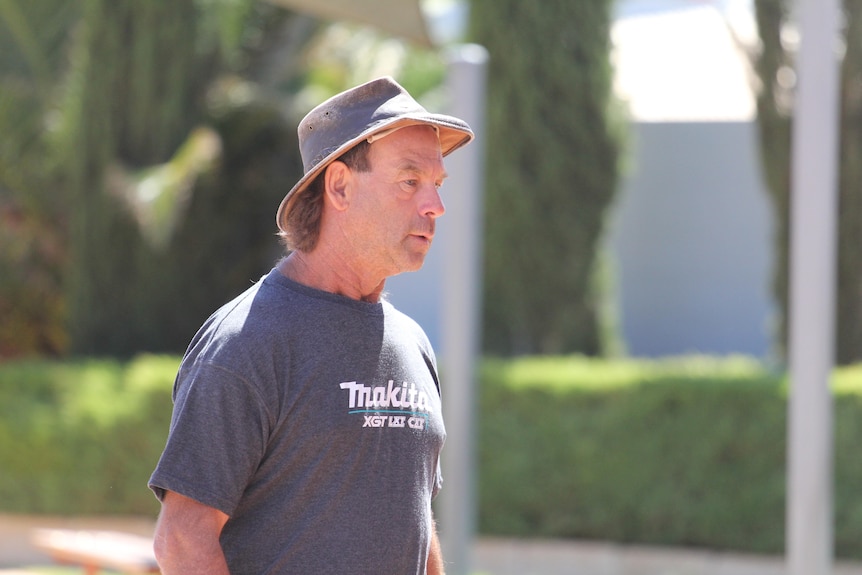 A man in wide-brim hat walking into a police station to report for bail for trial.  