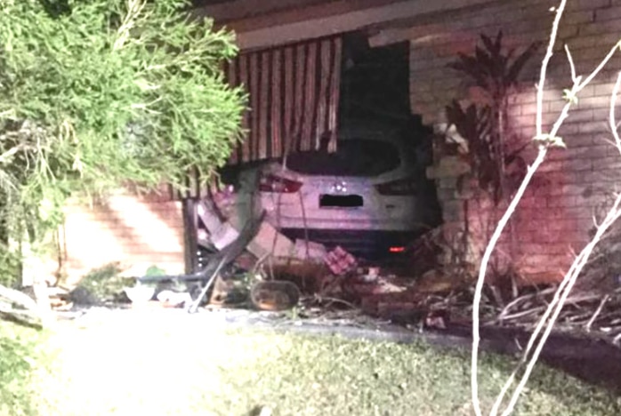 A white car that has crashed through the front of a brick house