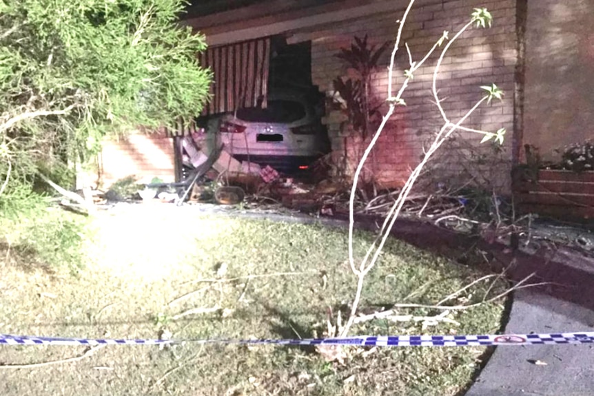 A white car that has crashed through the front of a brick house