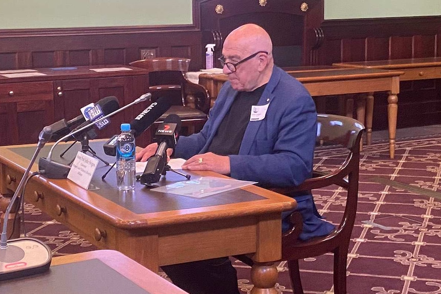 A man sits at a desk in a room with wood panelling and red carpet