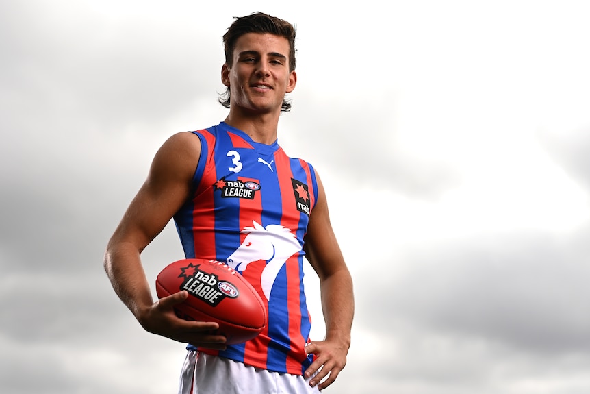 Nick Daicos poses for a photo wearing his Oakleigh Chargers jersey and holding a footy