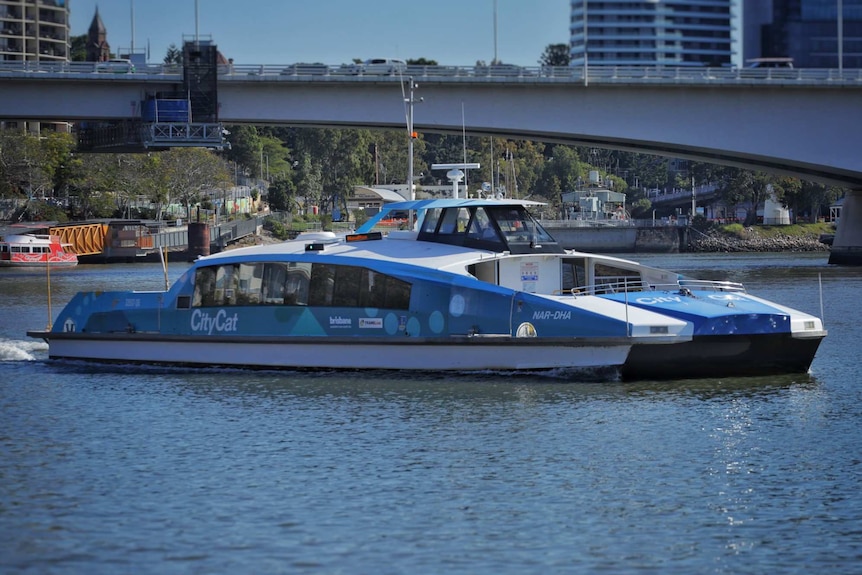 El ferry Blue City Cat llamado Nar-Dha en el río Brisbane, con la autopista South East Freeway y South Bank a la vista.