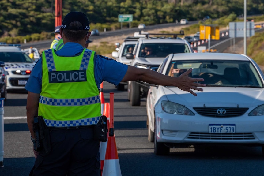 A police officer stands with his right arm extended flagging down a car on Forrest Highway.