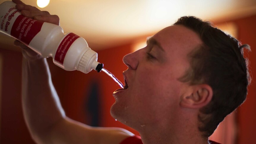 A footballer squirts water from a drink bottle into his mouth in the team clubrooms.