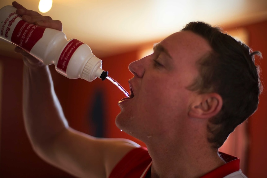 A footballer squirts water from a drink bottle into his mouth in the team clubrooms.