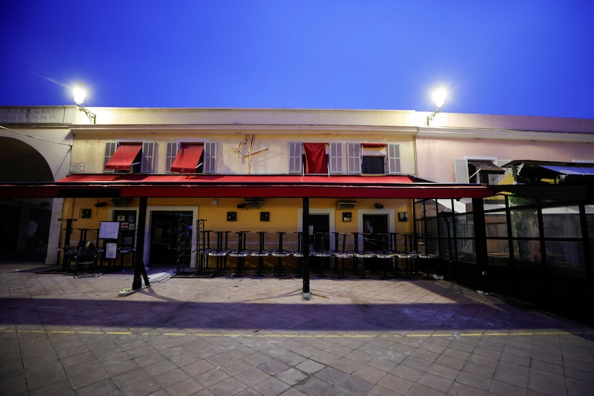 A European restaurant is deserted at night with tables stacked in front.