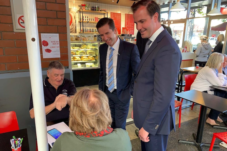 Two men in suits talking to people sitting down in a coffee shop