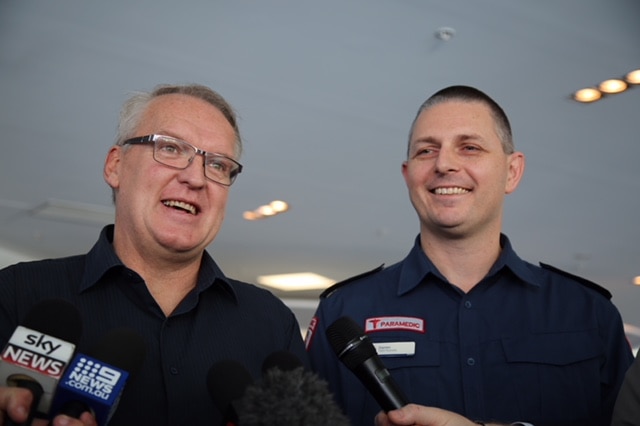 Keith Young and paramedic Darren speak behind media microphones.