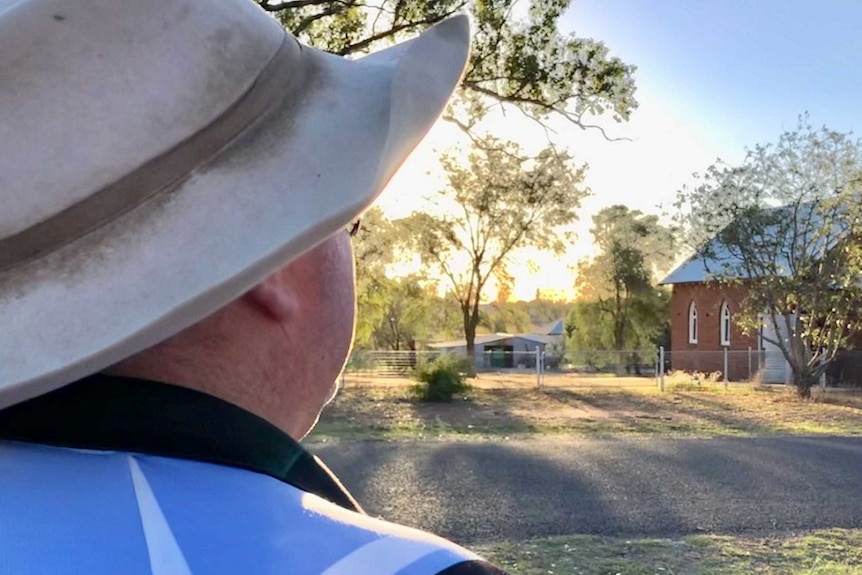 A farmer (unidentified) seen from behind with a church and sunset in the distance.