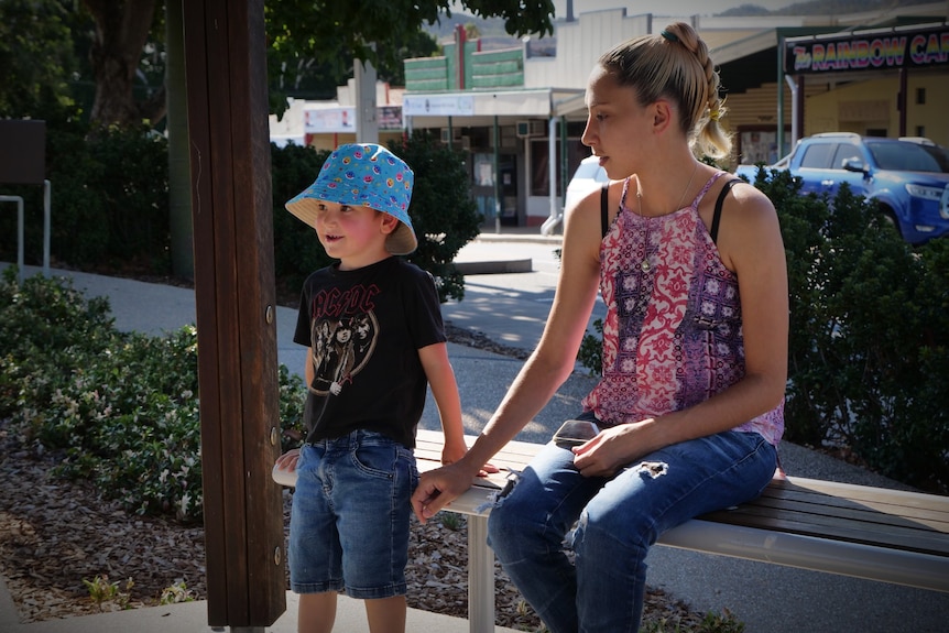 A woman sitting on a bench holding hands with a young boy wearing a blue hat