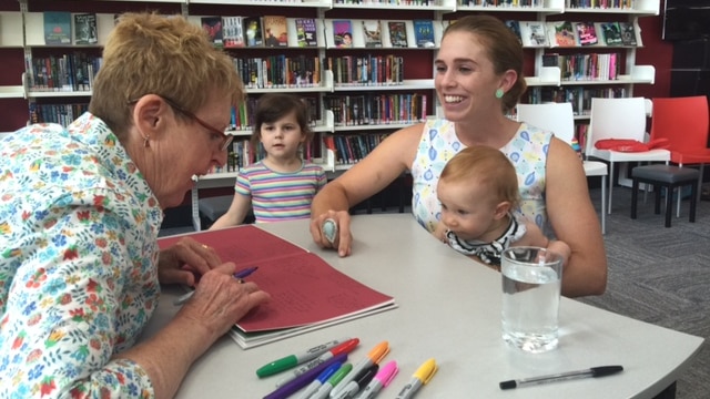 Mem Fox signs a book for a mother and small child.