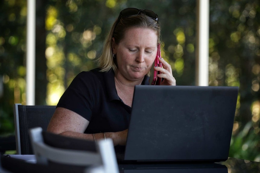 Kristy Aitken, looks serious as she listens on a mobile phone, sitting in front of a laptop computer.