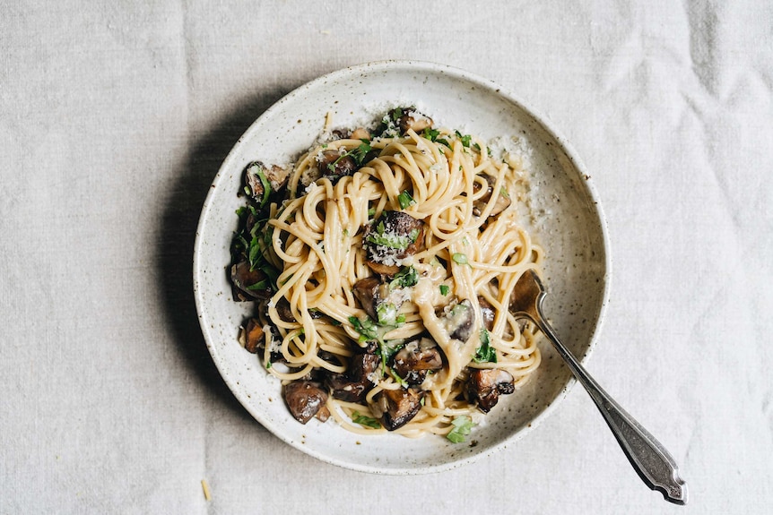 A plate of creamy mushroom and miso carbonara with Parmesan cheese and chopped parsley on top, a vegetarian pasta dinner.