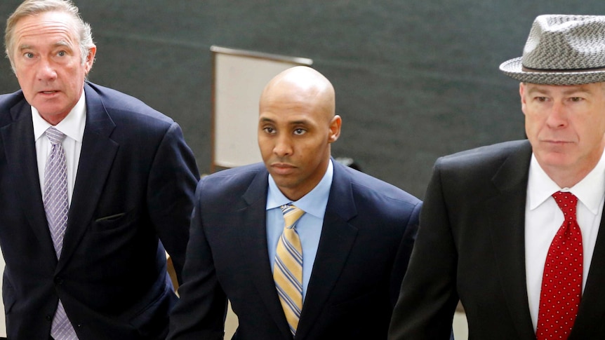 Mohamed Noor in a suit with a neutral expression walks, with members of his legal team on either side of him