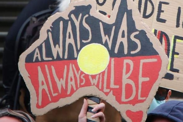 A protest sign reads 'Always Was Always Will Be', in front of police officers standing on Parliament's steps.