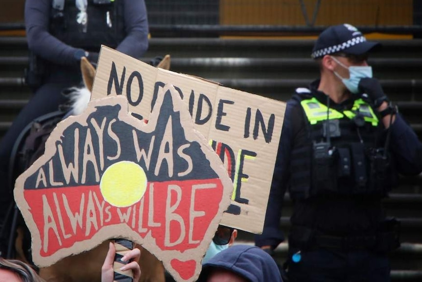 A protest sign reads 'Always Was Always Will Be', in front of police officers standing on Parliament's steps.