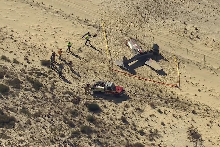 A crashed plane lies on sand is fenced off as emergency services work around it.