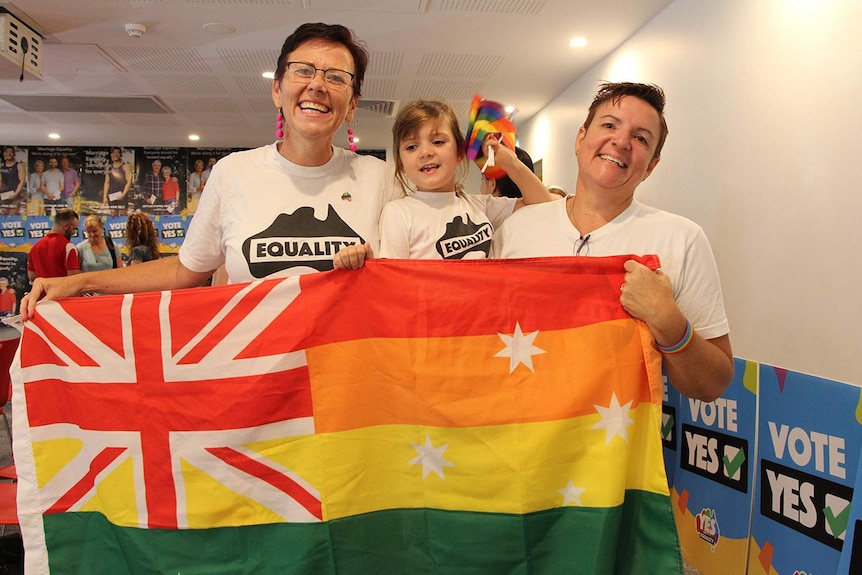 Kirsty Hunt, Amber Sayers, and Paige hold a rainbow banner