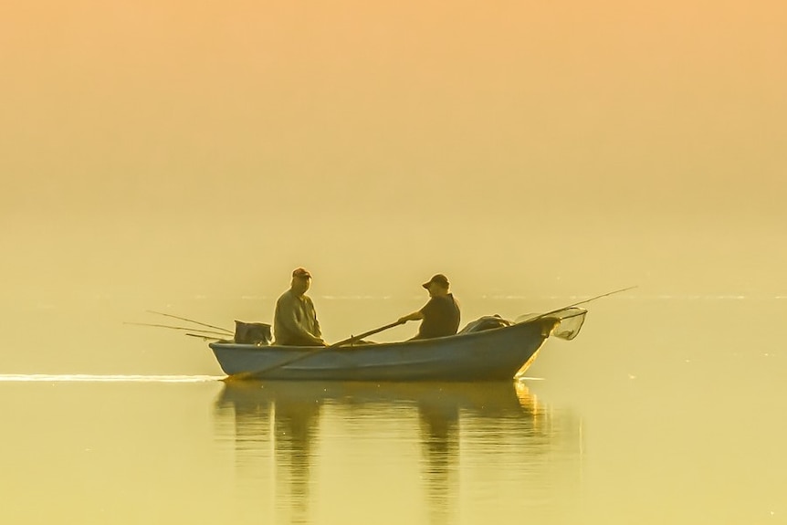 Two people in a small boat, fishing on a lake in golden light.