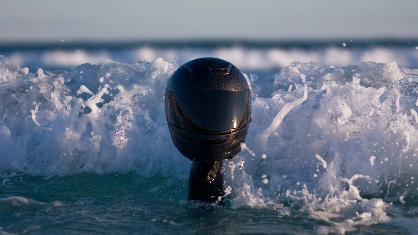 A motorcycle helmet is held above the ocean.