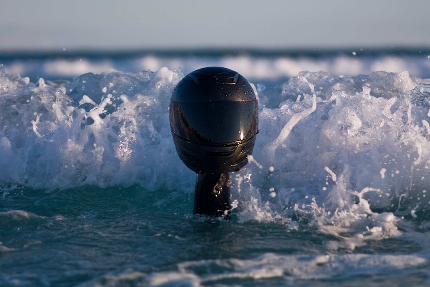A motorcycle helmet is held above the ocean.