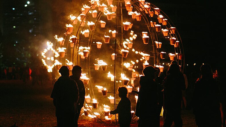 sphere of small flames with people in silhouette looking at it in darkness