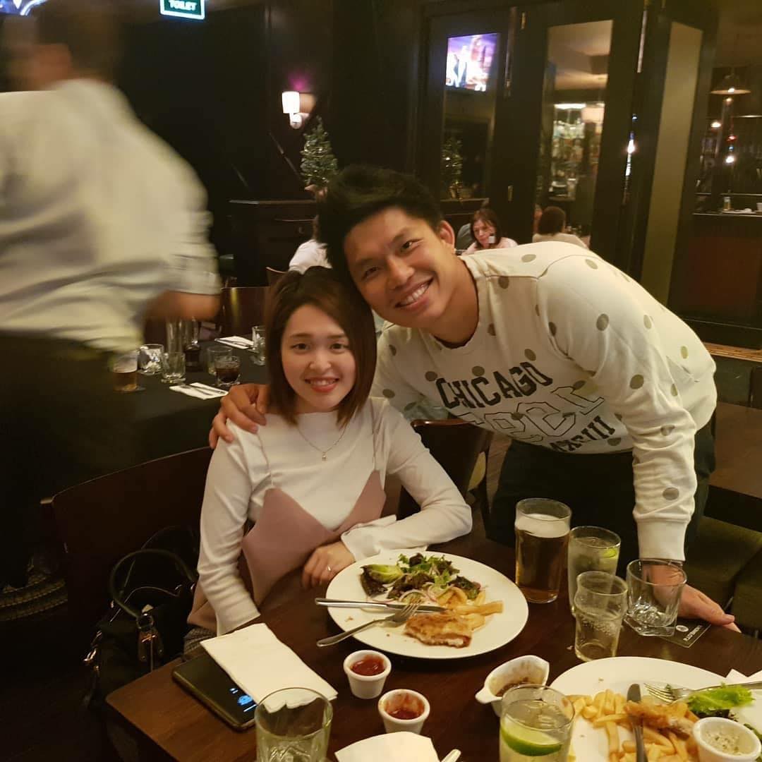 An Asian woman and man smile for a photo as their picture is taken at a restaurant