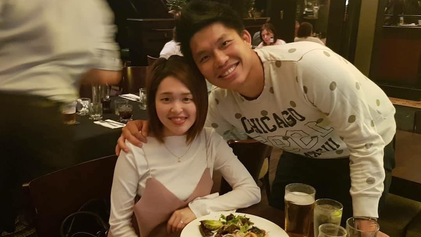 An Asian woman and man smile for a photo as their picture is taken at a restaurant