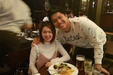 An Asian woman and man smile for a photo as their picture is taken at a restaurant
