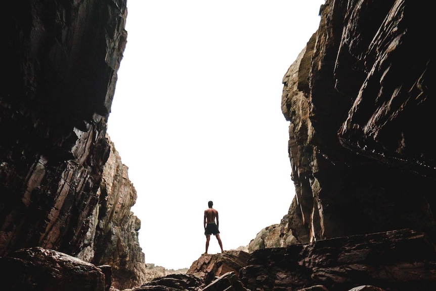 A person silhouetted against the entrance to a rocky cave.