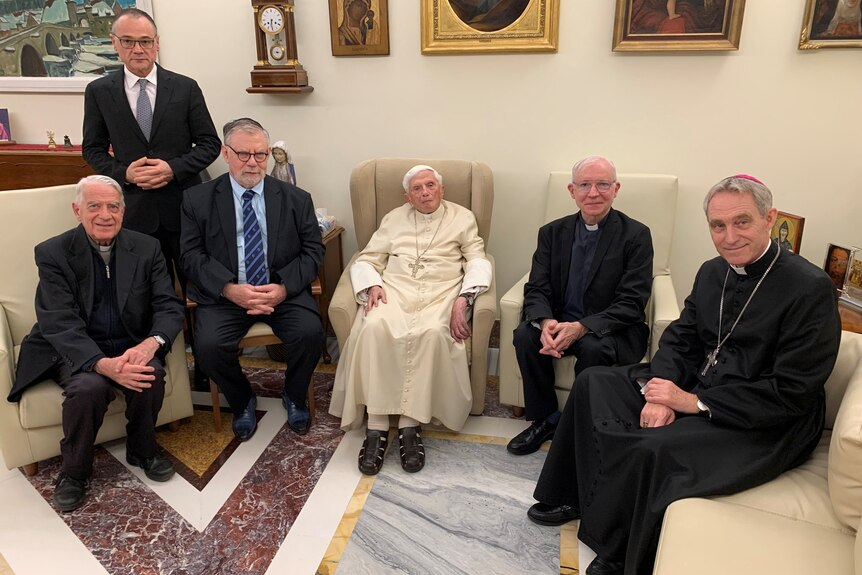 Five men sitting on seats with the former pope in the middle dressed in white